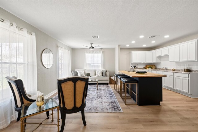 kitchen featuring light hardwood / wood-style flooring, ceiling fan, tasteful backsplash, white cabinetry, and butcher block counters