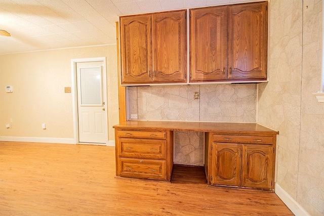 unfurnished office with light wood-type flooring, built in desk, and crown molding