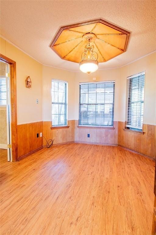 spare room with hardwood / wood-style flooring, wood walls, crown molding, and a textured ceiling