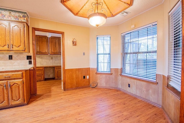 kitchen featuring a textured ceiling, light hardwood / wood-style floors, crown molding, and wood walls