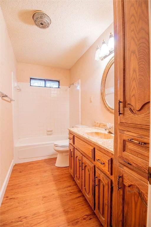 full bathroom featuring hardwood / wood-style floors, vanity, tiled shower / bath combo, toilet, and a textured ceiling