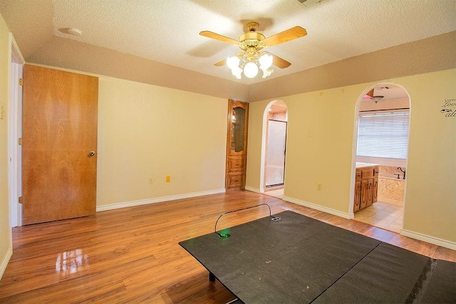 workout area with ceiling fan, light hardwood / wood-style flooring, and a textured ceiling