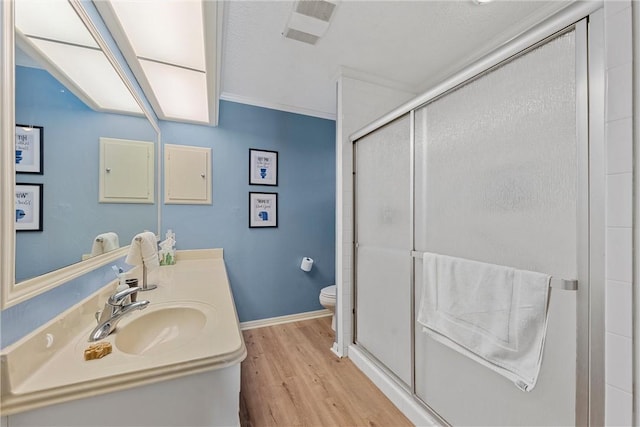 bathroom with vanity, a shower with door, hardwood / wood-style flooring, toilet, and ornamental molding