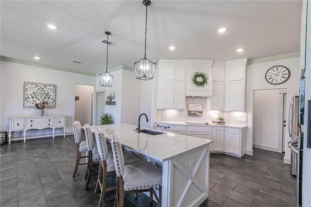 kitchen featuring light stone counters, a kitchen island with sink, sink, white cabinetry, and hanging light fixtures