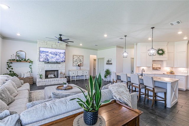 living room with ceiling fan, sink, dark hardwood / wood-style floors, crown molding, and a fireplace