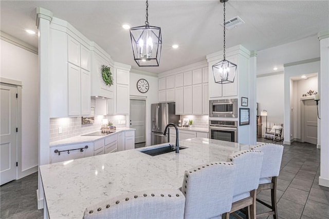 kitchen with sink, decorative backsplash, an island with sink, appliances with stainless steel finishes, and decorative light fixtures