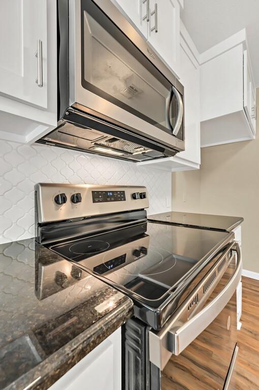 kitchen with white cabinets, light hardwood / wood-style flooring, decorative backsplash, dark stone countertops, and stainless steel appliances