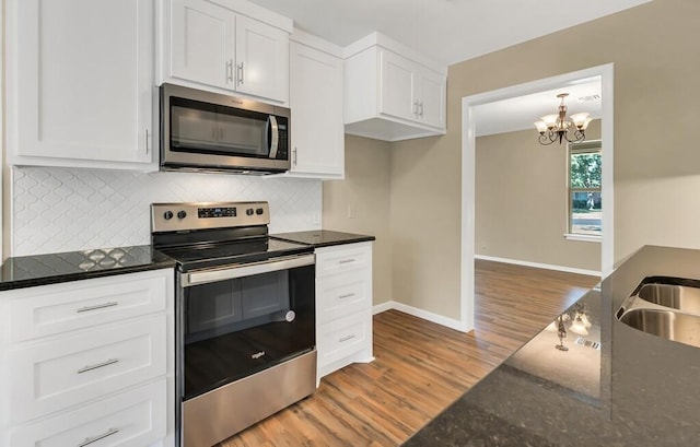 kitchen with dark stone counters, stainless steel appliances, dark wood-type flooring, a chandelier, and white cabinetry