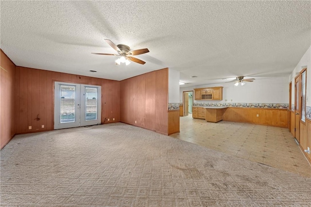 unfurnished living room with french doors, a textured ceiling, ceiling fan, and wood walls