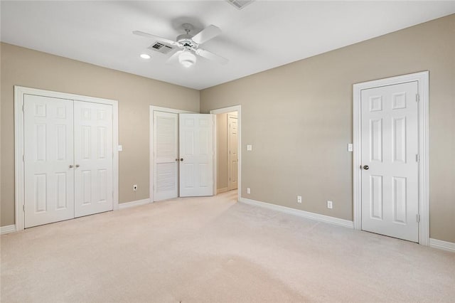 unfurnished bedroom with ceiling fan, light colored carpet, and two closets