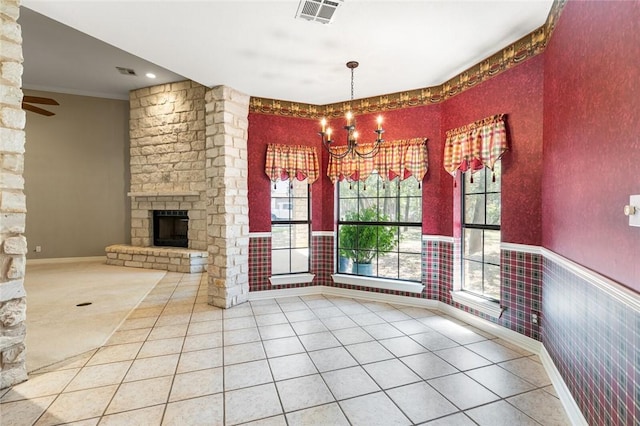 unfurnished dining area featuring tile patterned floors, ceiling fan with notable chandelier, crown molding, and a fireplace