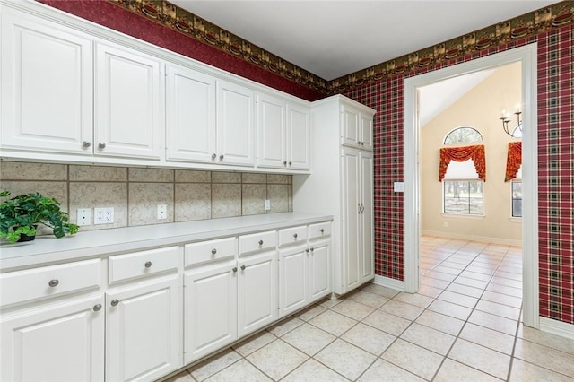 kitchen with backsplash, white cabinetry, light tile patterned floors, and lofted ceiling