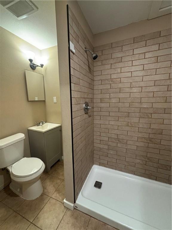 bathroom with tiled shower, vanity, toilet, and tile patterned flooring