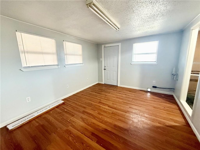 unfurnished room with wood-type flooring, a baseboard heating unit, and a textured ceiling