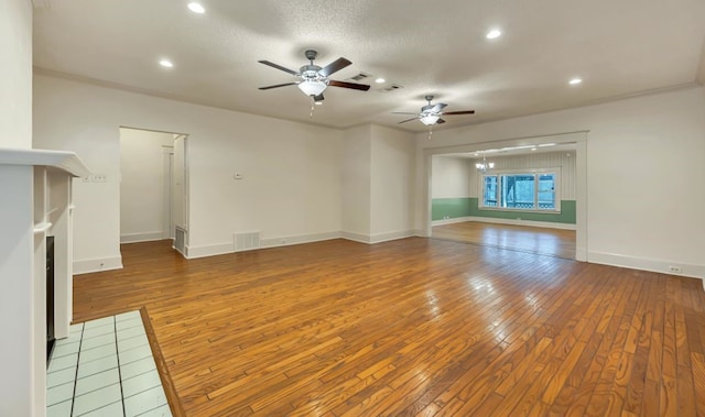 unfurnished living room featuring ceiling fan, a tile fireplace, hardwood / wood-style floors, and a textured ceiling