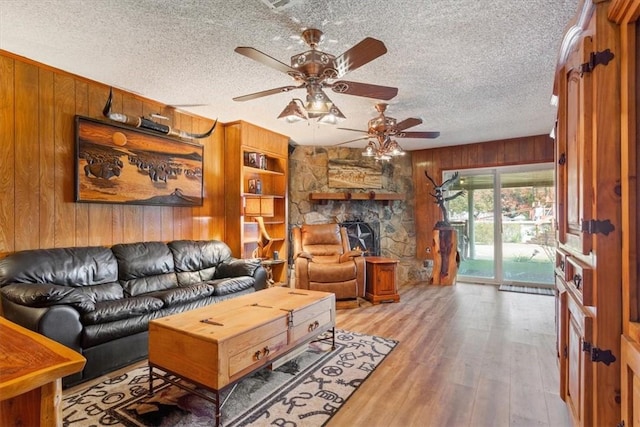 living room featuring wooden walls, ceiling fan, light hardwood / wood-style floors, and a textured ceiling