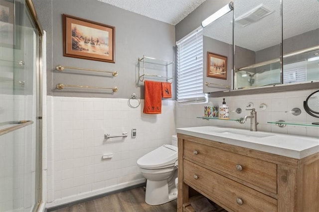 bathroom featuring vanity, a textured ceiling, hardwood / wood-style flooring, tile walls, and toilet