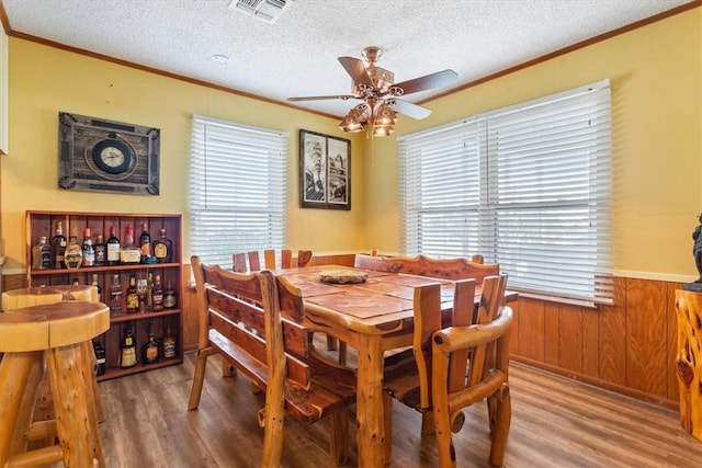 dining space with ceiling fan, crown molding, light hardwood / wood-style floors, a textured ceiling, and wooden walls