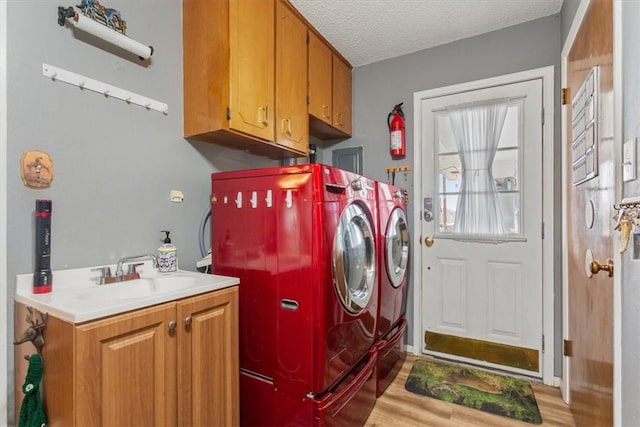 clothes washing area featuring sink, cabinets, washing machine and dryer, a textured ceiling, and light wood-type flooring