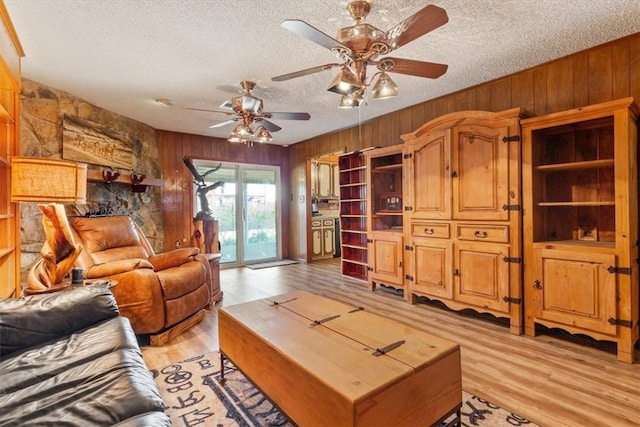 living room featuring wood walls, ceiling fan, light hardwood / wood-style floors, and a textured ceiling