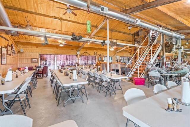 dining area featuring wood walls, ceiling fan, and concrete flooring