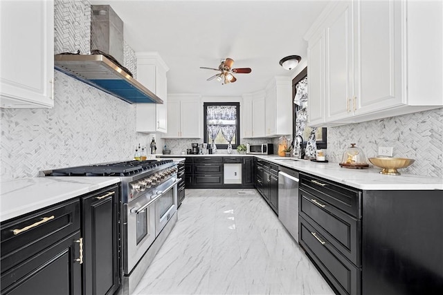 kitchen featuring wall chimney exhaust hood, stainless steel appliances, ceiling fan, sink, and white cabinets