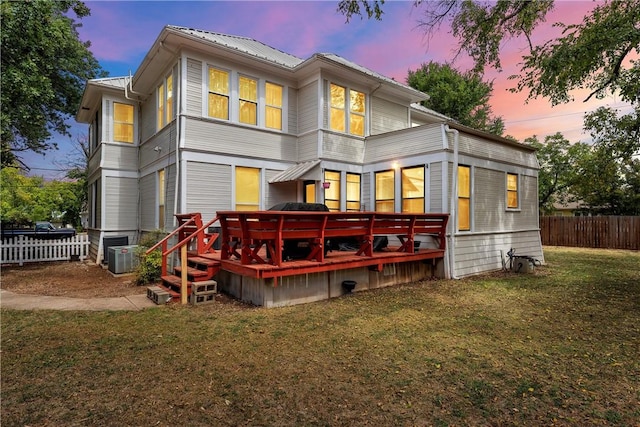 back house at dusk featuring a lawn and a wooden deck