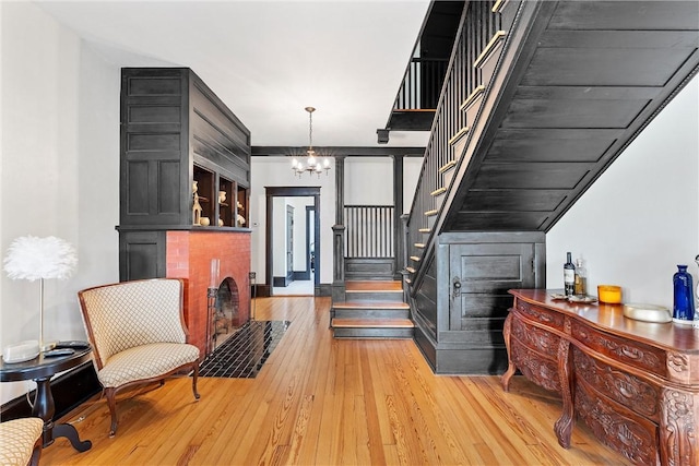 staircase featuring hardwood / wood-style flooring, a brick fireplace, and a notable chandelier