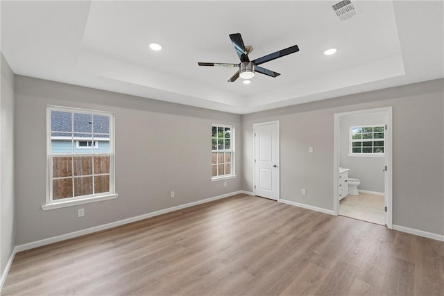 unfurnished bedroom with multiple windows, ensuite bathroom, and light hardwood / wood-style floors