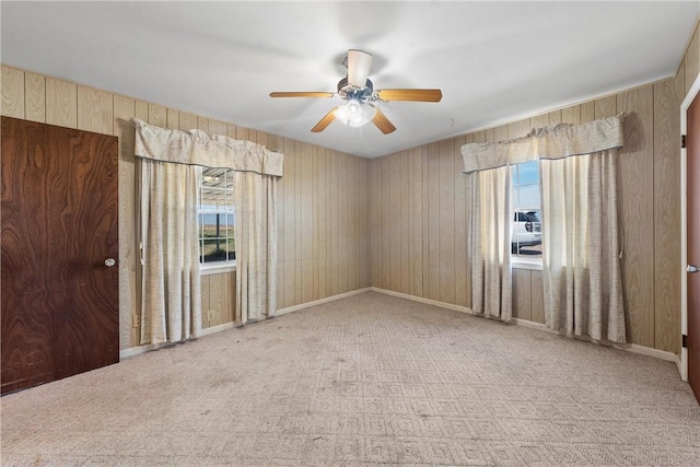 carpeted spare room with wooden walls and ceiling fan