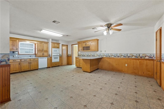 kitchen featuring a textured ceiling, white appliances, ceiling fan, kitchen peninsula, and wood walls