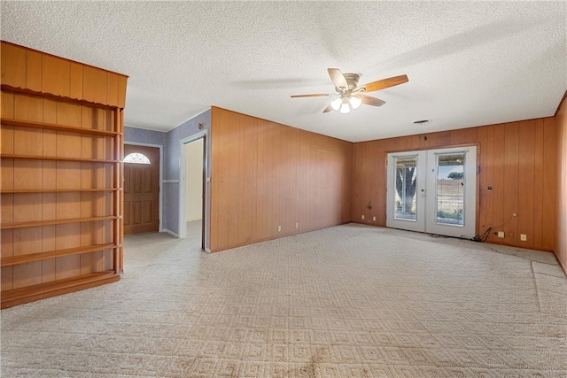 spare room with a textured ceiling, french doors, ceiling fan, and wooden walls