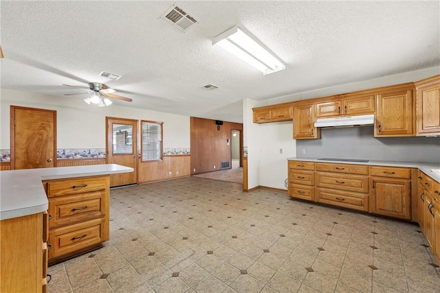 kitchen with ceiling fan, a textured ceiling, wood walls, and black electric stovetop