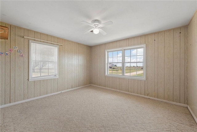 unfurnished room featuring ceiling fan, light carpet, and wood walls