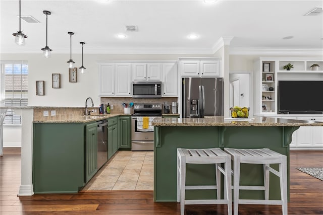 kitchen with a kitchen bar, a sink, stainless steel appliances, green cabinets, and white cabinets