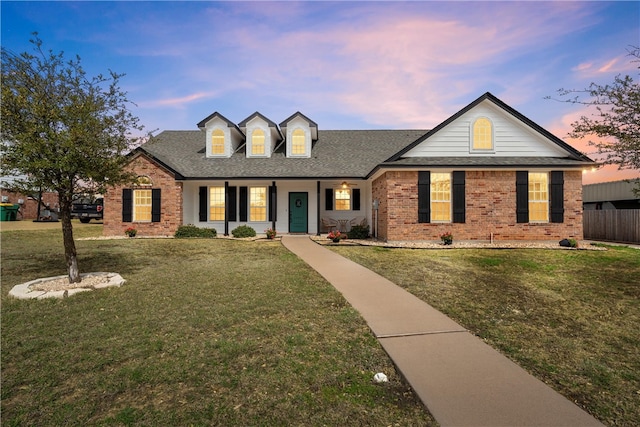 view of front of home with a front yard, fence, brick siding, and a shingled roof