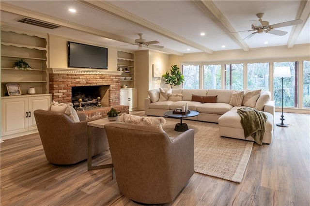 living room with beam ceiling, a brick fireplace, dark wood-type flooring, and plenty of natural light