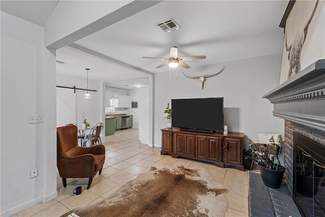 tiled living room with a barn door, ceiling fan, and a fireplace