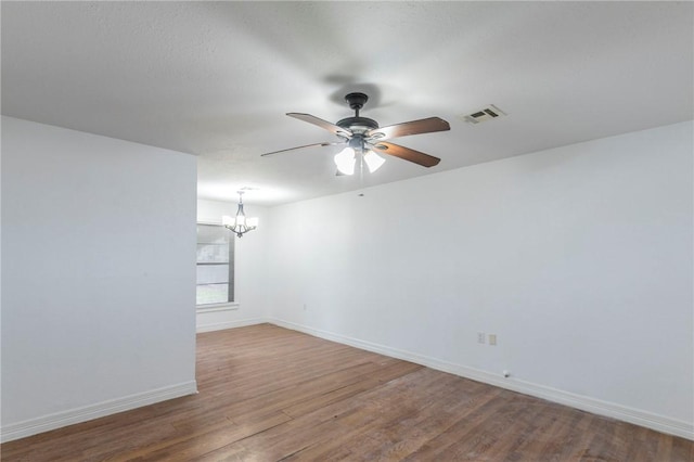 empty room featuring ceiling fan with notable chandelier and hardwood / wood-style floors