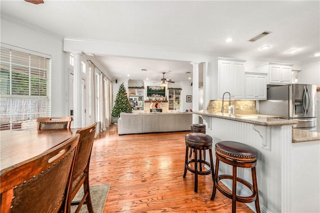 kitchen with white cabinetry, ceiling fan, stainless steel fridge, a breakfast bar area, and light wood-type flooring