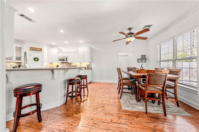 bar with ornamental molding, white cabinets, and light wood-type flooring