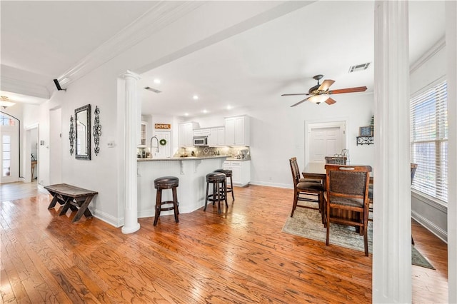 dining space featuring light hardwood / wood-style floors, ceiling fan, ornamental molding, and decorative columns