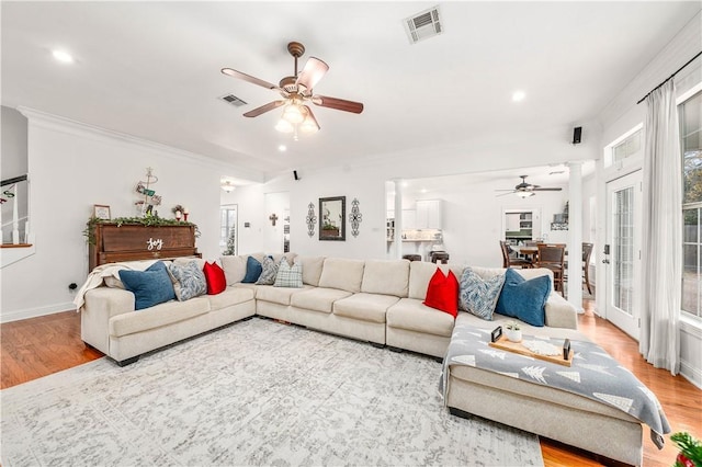 living room featuring light wood-type flooring, decorative columns, ceiling fan, and ornamental molding