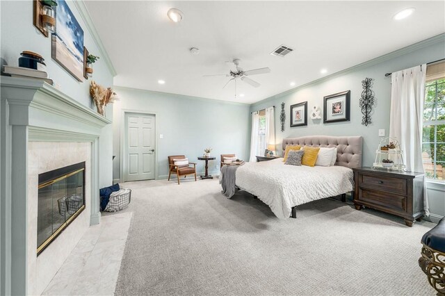 carpeted bedroom with connected bathroom, a tiled fireplace, ceiling fan, and crown molding