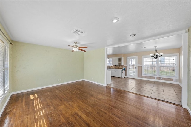 unfurnished living room featuring baseboards, visible vents, wood finished floors, and ceiling fan with notable chandelier