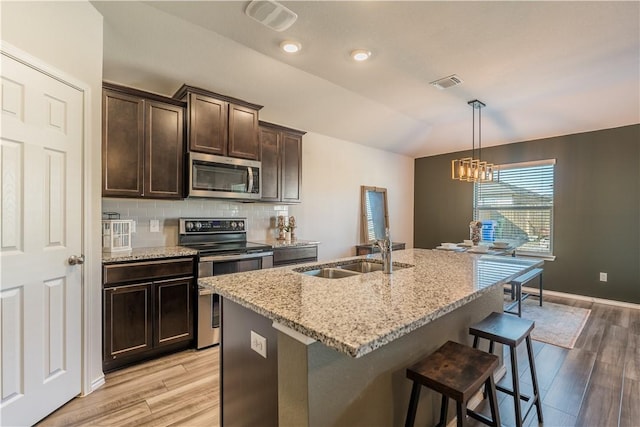 kitchen with appliances with stainless steel finishes, sink, light hardwood / wood-style floors, and an island with sink