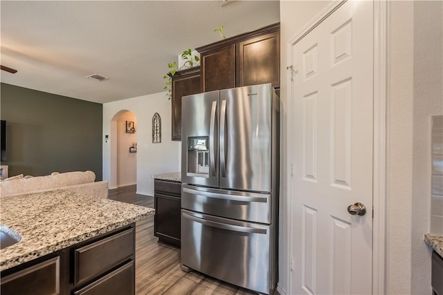 kitchen with dark brown cabinetry, stainless steel fridge, light stone countertops, and light wood-type flooring