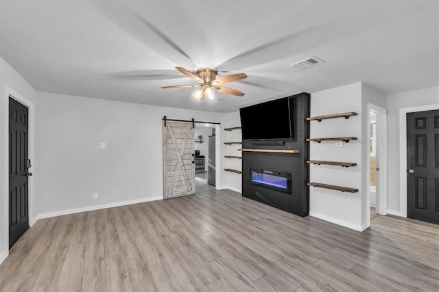 unfurnished living room with a fireplace, a barn door, light hardwood / wood-style floors, and ceiling fan