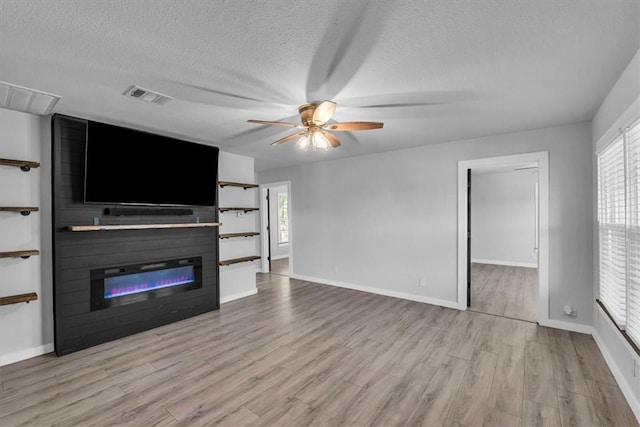 unfurnished living room with ceiling fan, a large fireplace, light wood-type flooring, and a textured ceiling