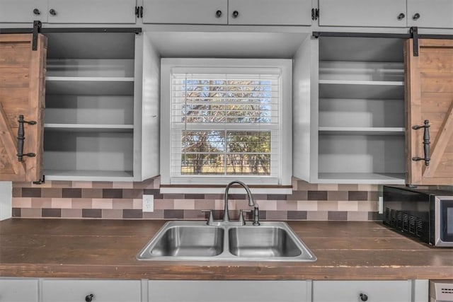 kitchen with backsplash, a barn door, white cabinets, and sink